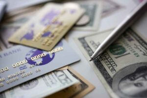 Banking plastic card and silver pen lying on big amount of US money closeup