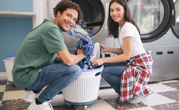 Happy Couple Doing Laundry Loading Washer Machine At Laundromat Room