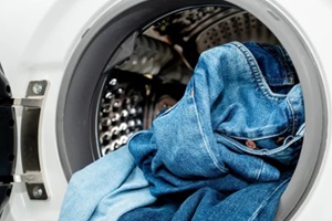 pile of jeans in the drum of open washing machine in laundry room