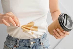 young woman with coffee stains on her t-shirt on light background