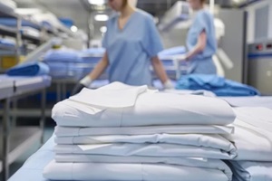 industrial laundry equipment with stack of folded clean sheets and surgical clothes